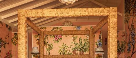 Una cama con dosel adornada con un dosel tejido, una lámpara colgante grande y un muro con estampado floral.