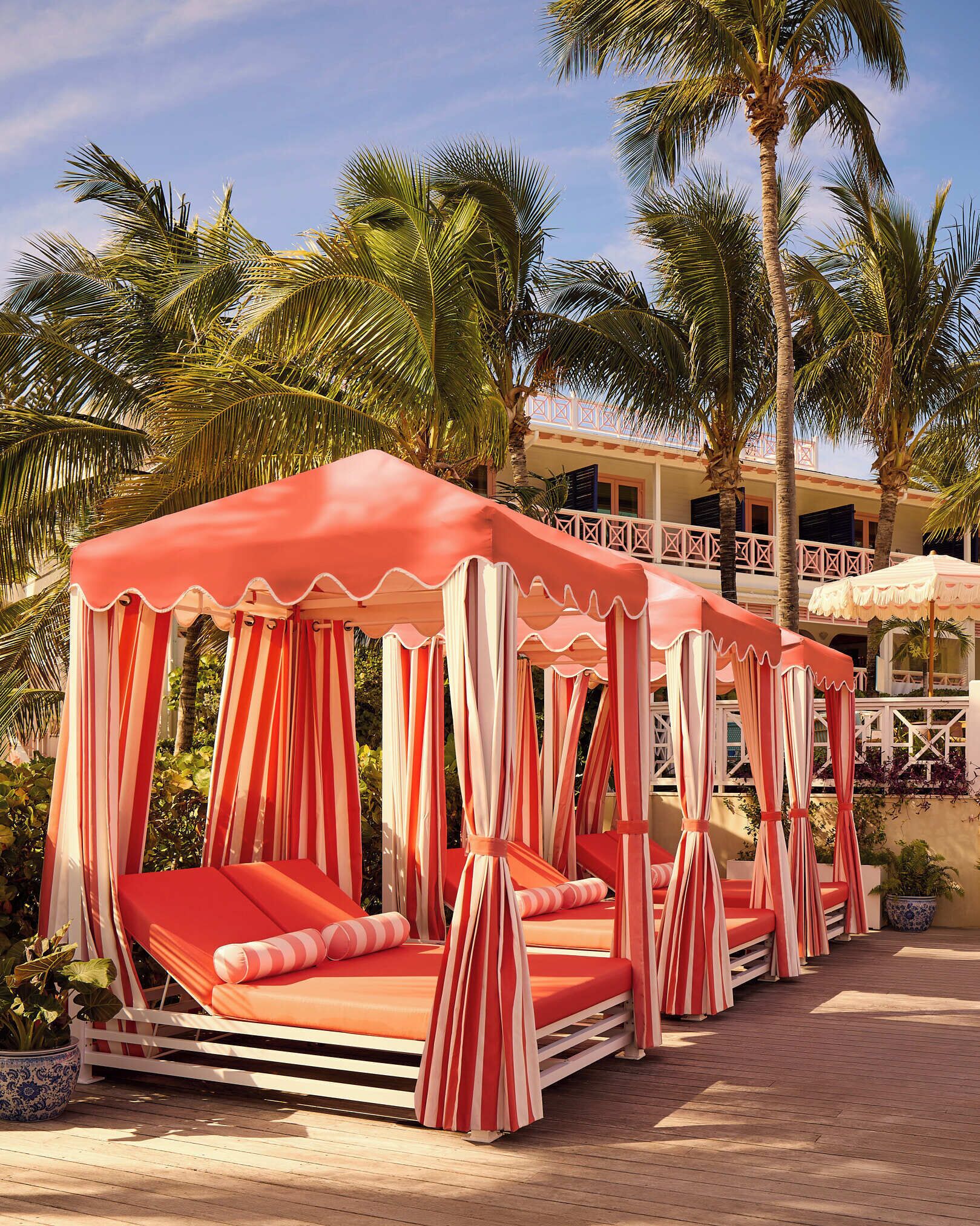 A row of red and white striped canopy beds with a wooden deck and palm trees in the background.