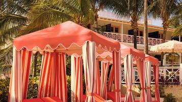 A row of red and white striped canopy beds with a wooden deck and palm trees in the background.