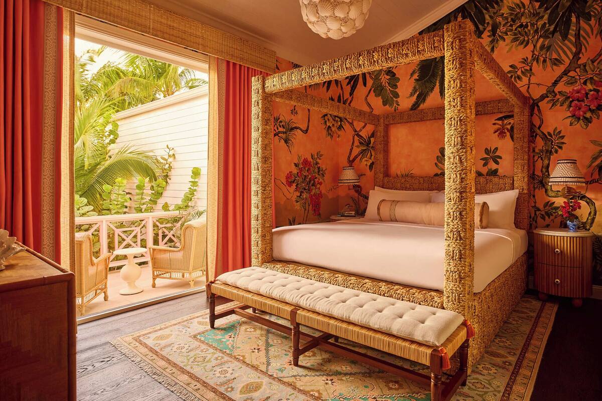 A four-poster bed with a bench, a small table, and a lamp on a nightstand.