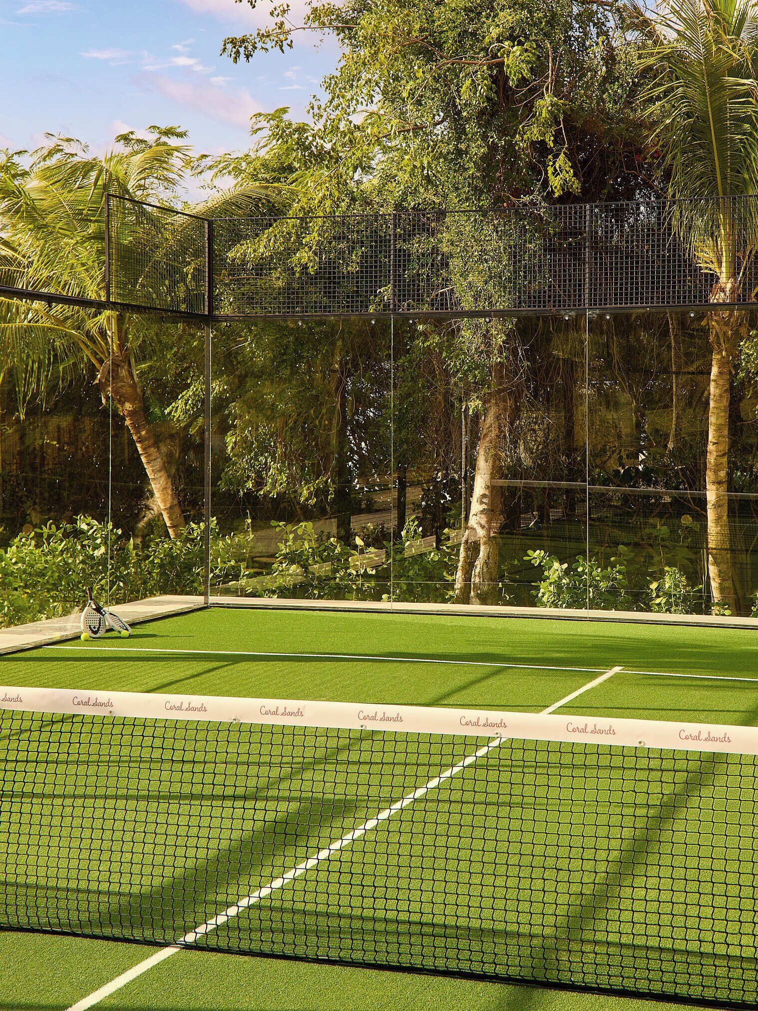 A tennis court with a net, surrounded by a fence and trees.