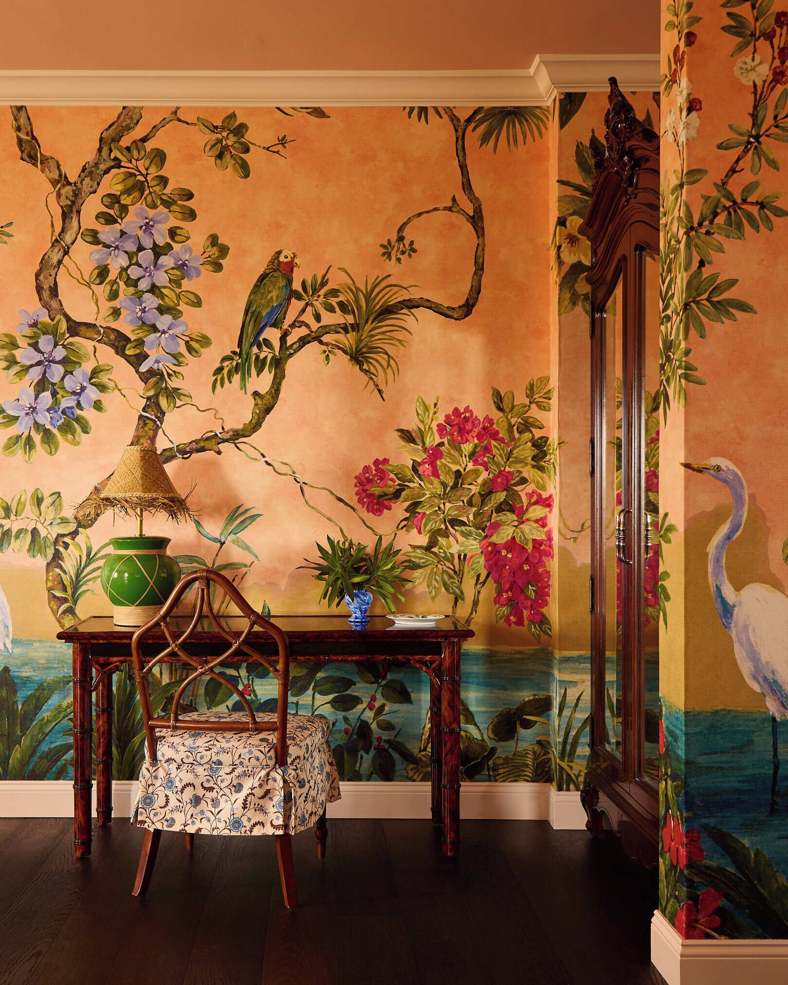 A room with a mural of tropical flora and fauna, a wooden table with a chair, and a large mirror.