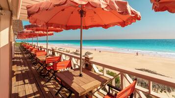 Terraza de madera con sillas y sombrillas anaranjadas con vista a una playa.