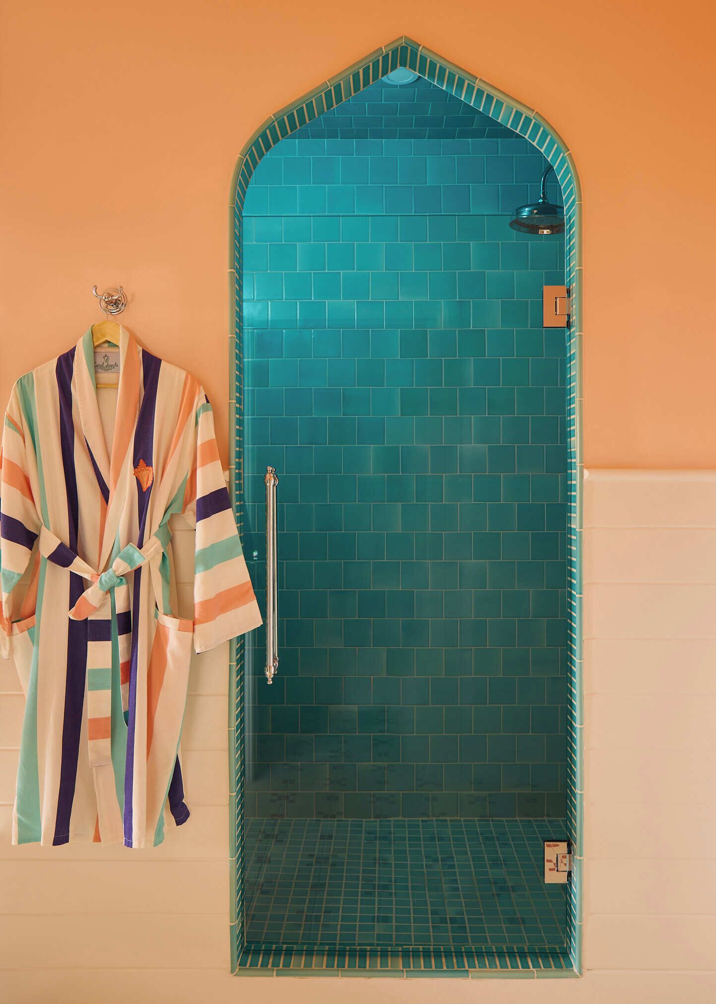 A bathroom with a shower area, a towel rack, and a tiled wall.