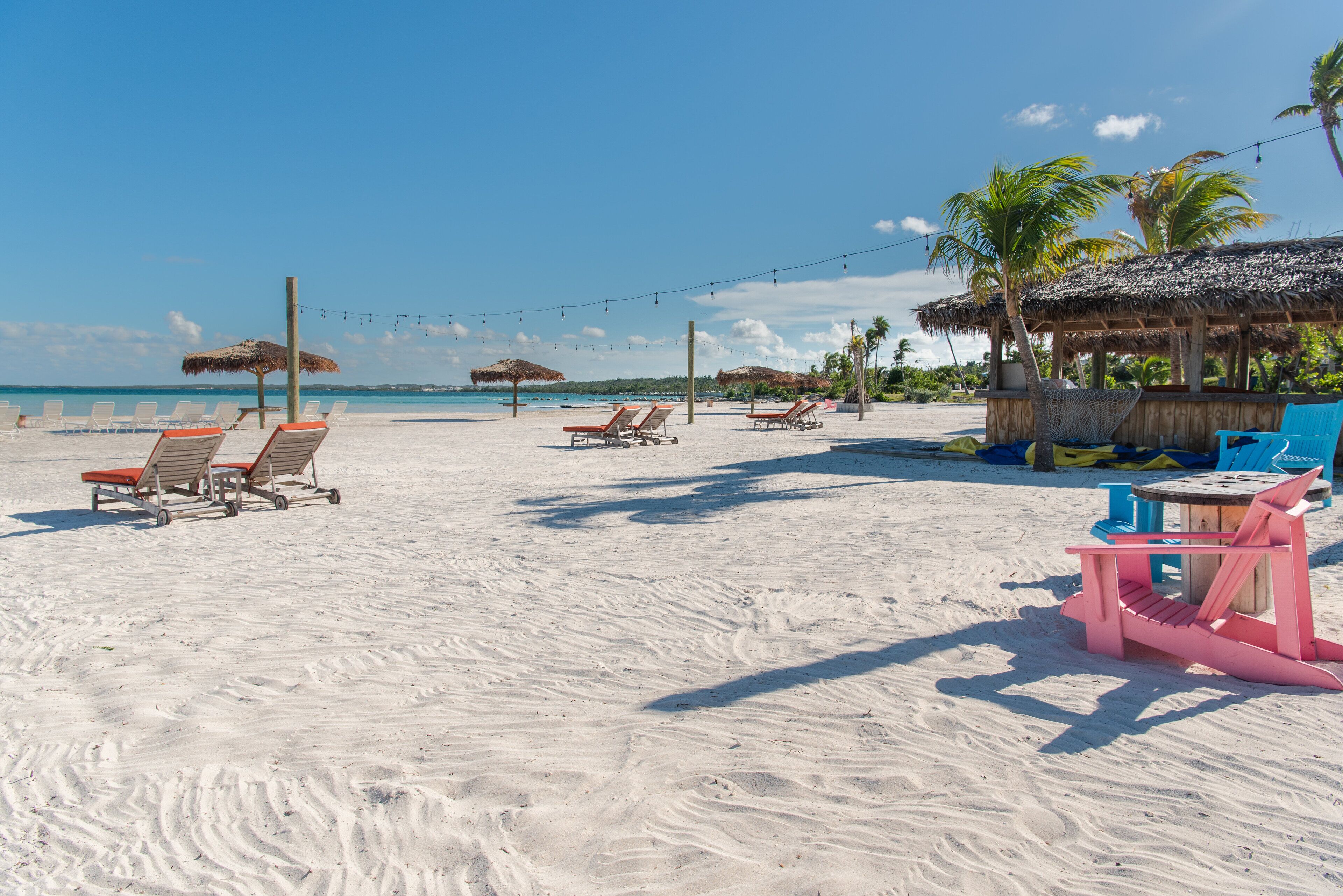 A beach with sun loungers, thatched umbrellas, and a small hut.