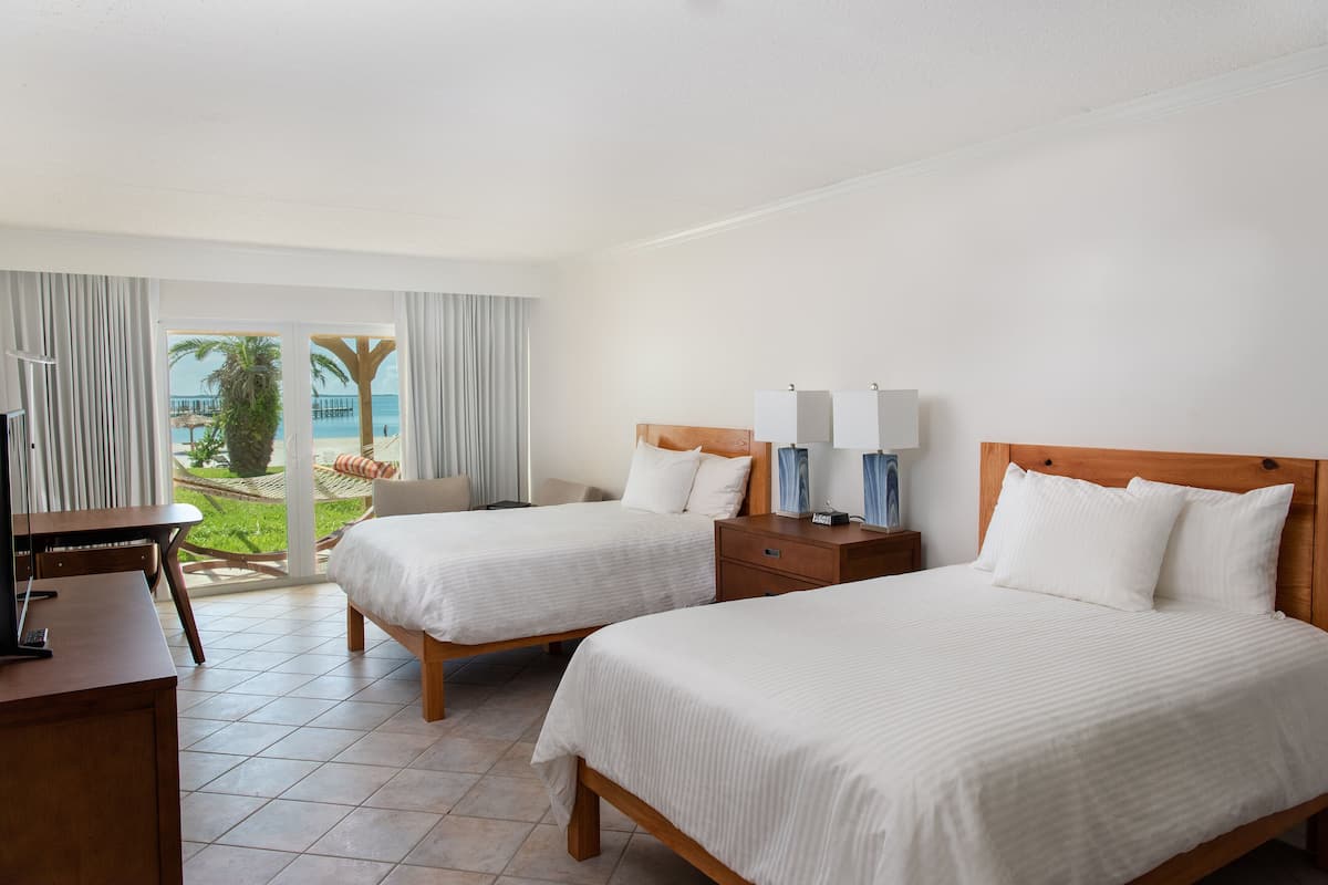 Habitación de hotel con dos camas, un escritorio y vista a la playa.