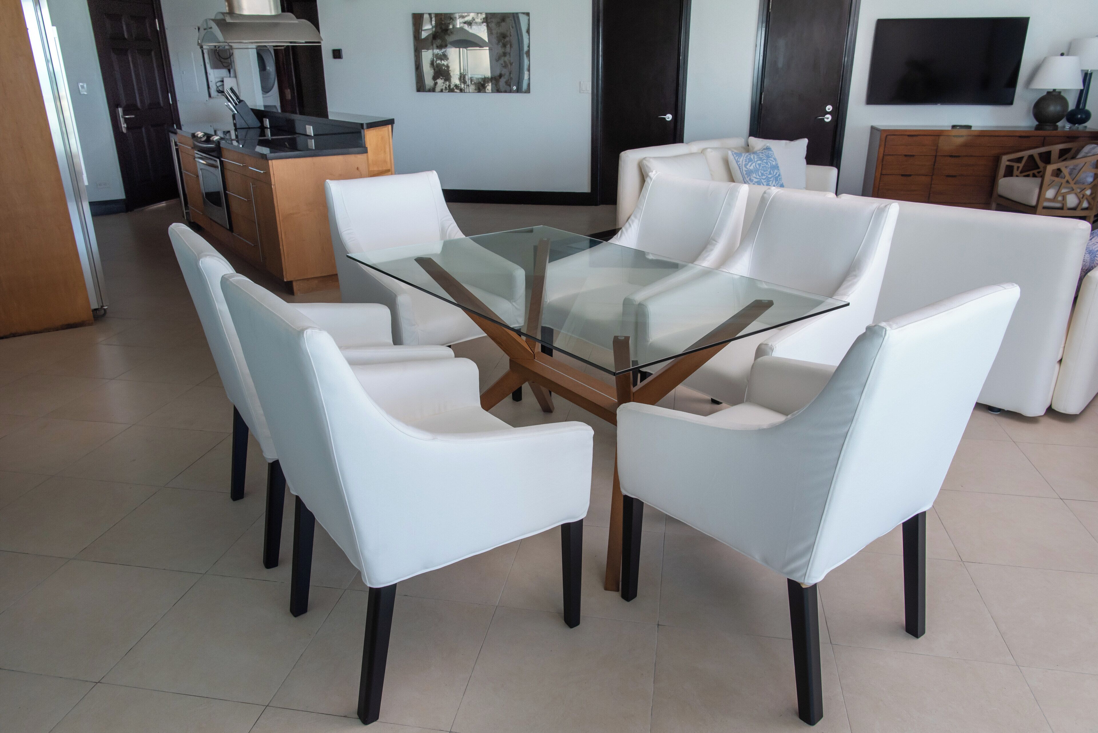 Un espace repas moderne avec une table à plateau de verre entourée de chaises blanches.