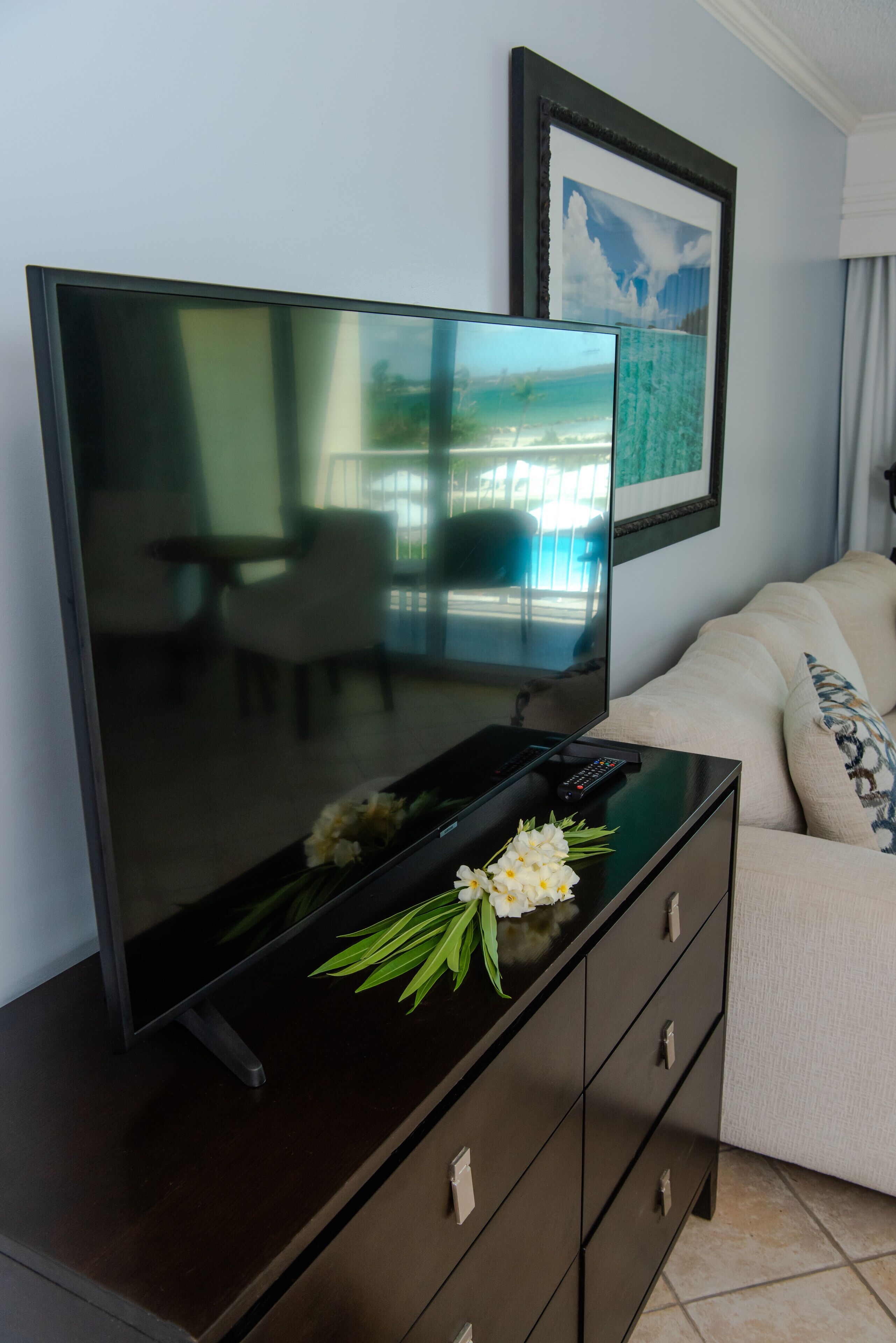 Un televisor de pantalla plana sobre un aparador de madera oscura, con un control remoto, un ramo de flores y un cuadro en la pared.
