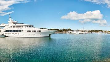 A large white yacht docked at a marina with clear turquoise water, surrounded by rocky shores and other boats.