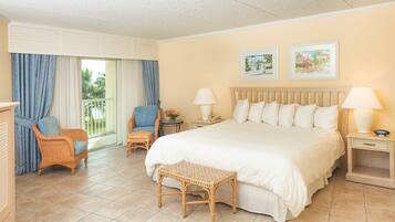 A hotel room with a large bed, two chairs, a small table, and a window with curtains.