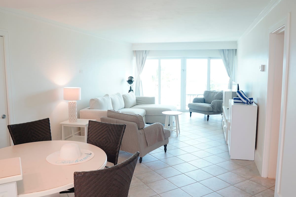 Una sala de estar moderna con un sofá, una mesa de comedor con sillas, una mesita blanca y una lámpara.
