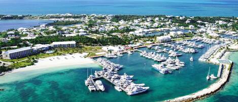An aerial view of a marina with numerous boats docked, a sandy beach, and surrounding residential buildings.