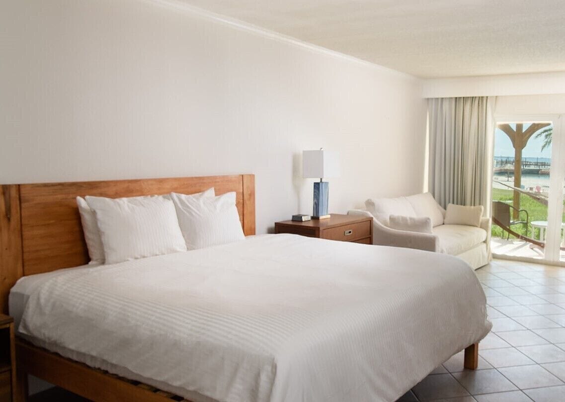 A hotel room with a large bed, a nightstand, a chair, and a view of the outdoors.