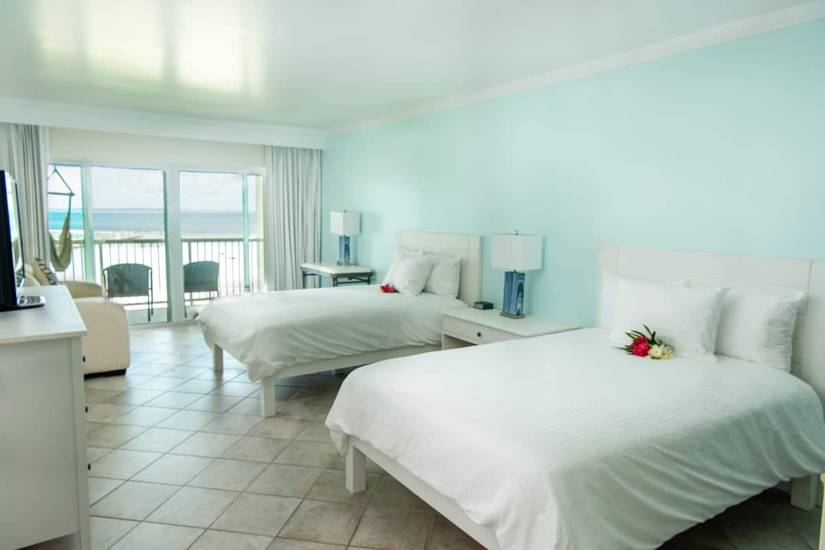 Habitación de hotel con dos camas, un escritorio, una silla, televisión y balcón con vista al mar.