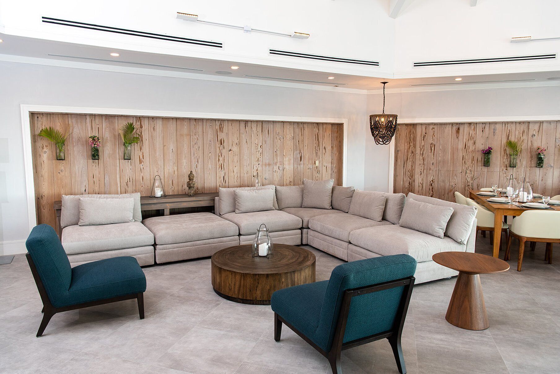 Uma sala de estar moderna com sofá de canto, duas poltronas, uma mesa de centro e uma área de jantar com mesa e cadeiras de madeira.