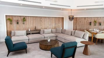 A modern living room with a sectional sofa, two armchairs, a coffee table, and a dining area with a wooden table and chairs.
