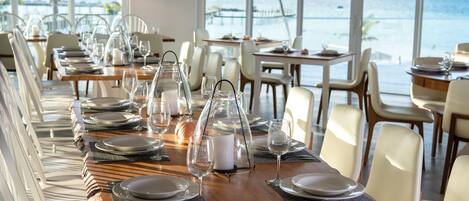 Comedor con mesas dispuestas para el servicio, con vistas a un paisaje marino.