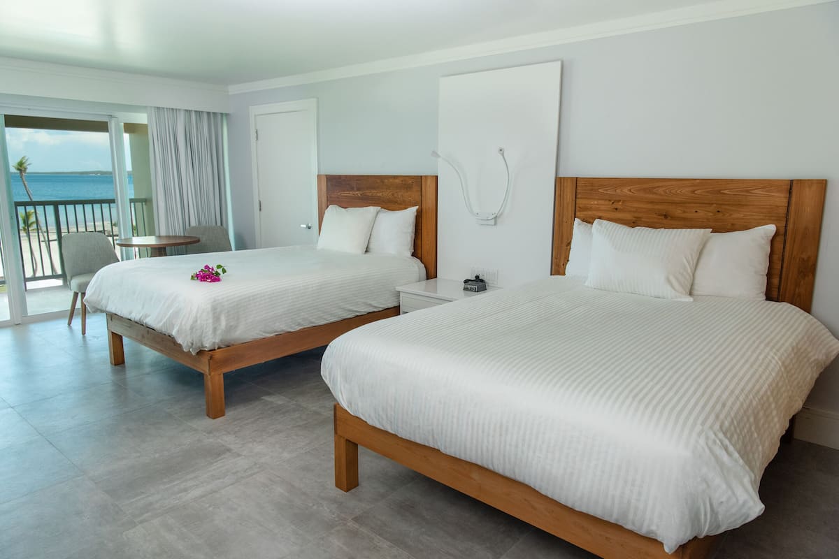 Habitación de hotel con dos camas, un balcón con vistas al mar y una pequeña mesa con sillas.