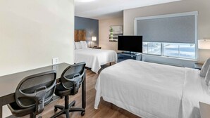A hotel room with two beds, a desk with chairs, a TV, and a window with a view.