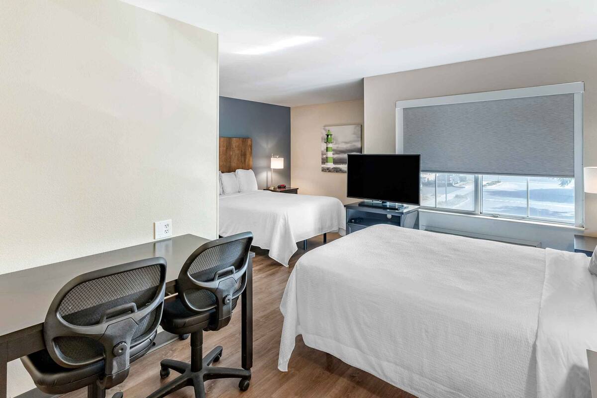 Een hotelkamer met twee bedden, een bureau met stoelen, een televisie en een raam met uitzicht.