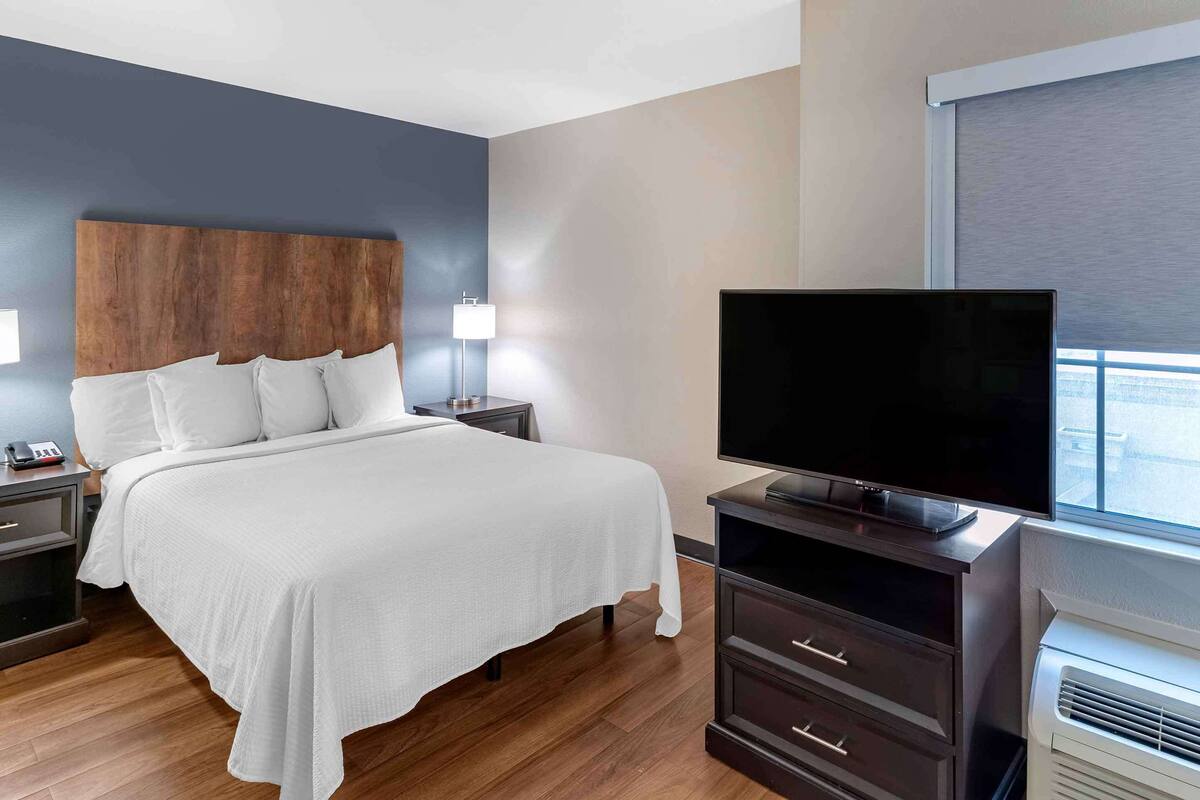 Une chambre d’hôtel moderne dotée d’un grand lit, de lampes de chevet, d’un téléviseur à écran plat, d’une commode et d’un appareil de climatisation.