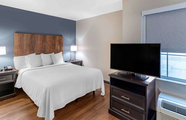 Una habitación de hotel moderna con una cama grande, lámparas de noche, un televisor de pantalla plana, un aparador y un equipo de aire acondicionado.