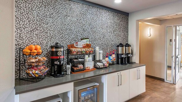 A breakfast bar with coffee makers, a fruit basket, and a refrigerator.