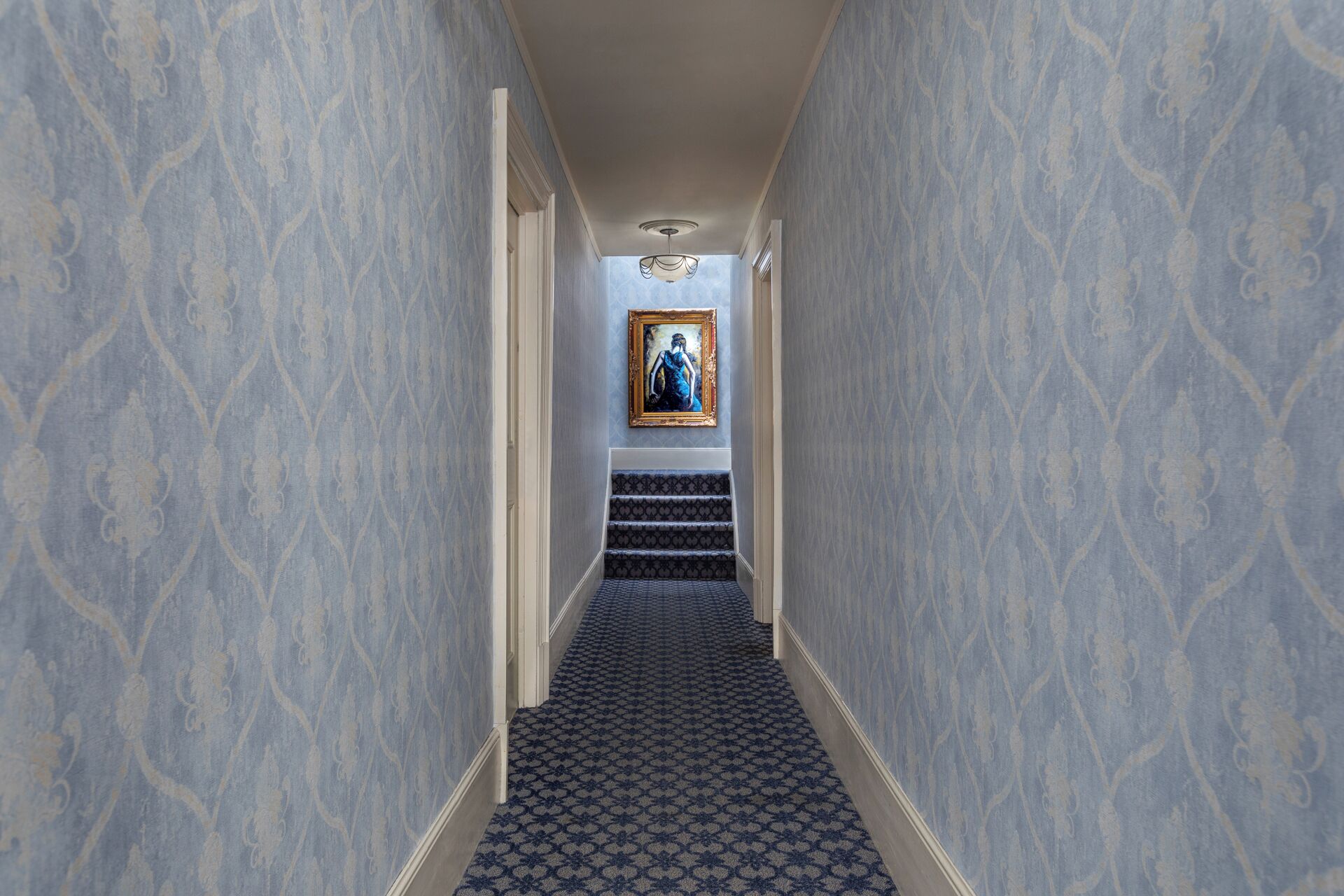 A hallway with patterned wallpaper, a staircase, and a framed painting on the wall.
