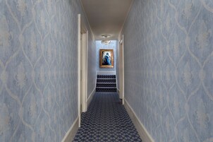 A hallway with patterned wallpaper, a staircase, and a framed painting on the wall.