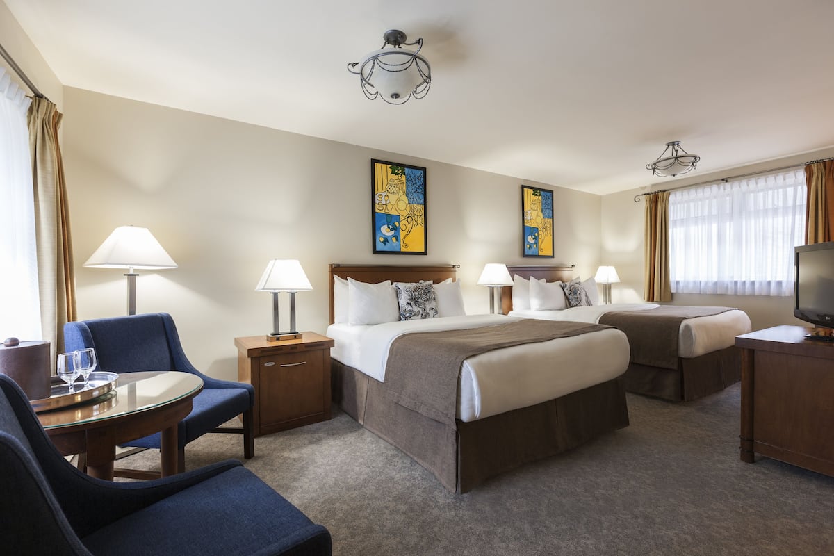 A hotel room with two beds, a desk, a chair, and a TV.