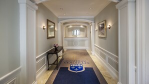 A hallway with a carpet featuring a coat of arms, white walls, and a framed picture on the right. - Chateau Versailles (Montreal)