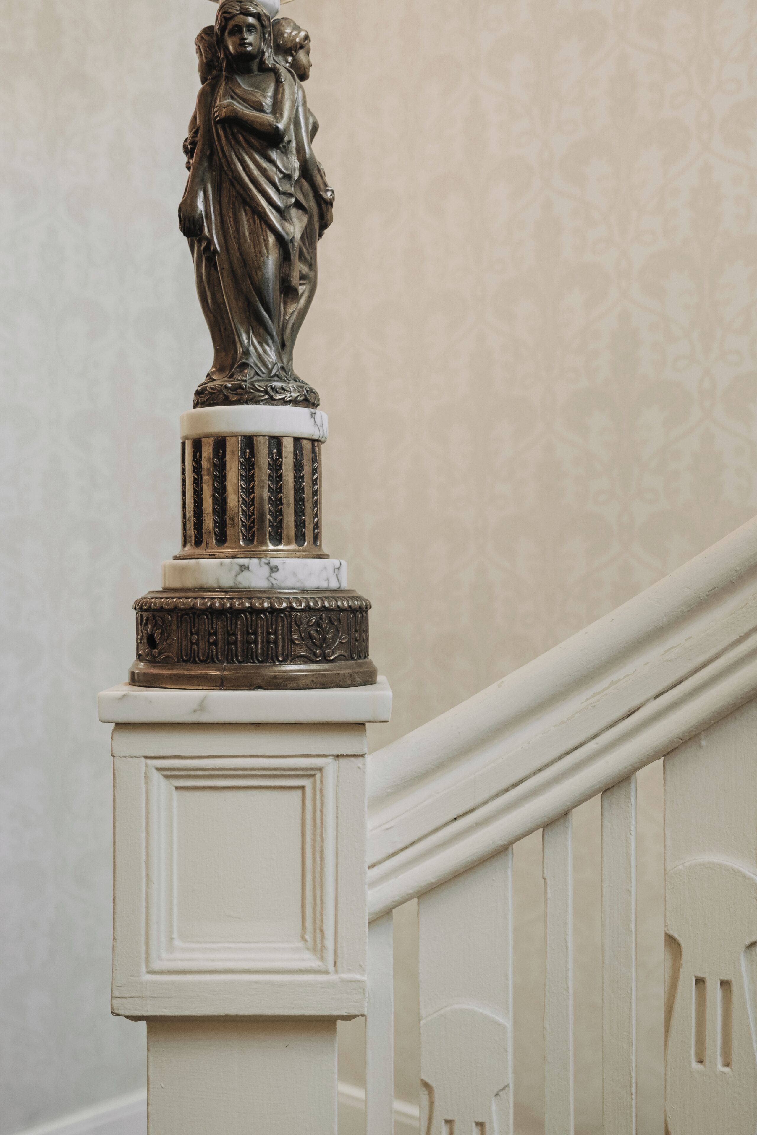 A statue on a white column with a patterned wall in the background.