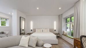 A modern bedroom with a large bed, a sofa, a small table, and a window with a view of greenery. - Chateau Versailles (Montreal)