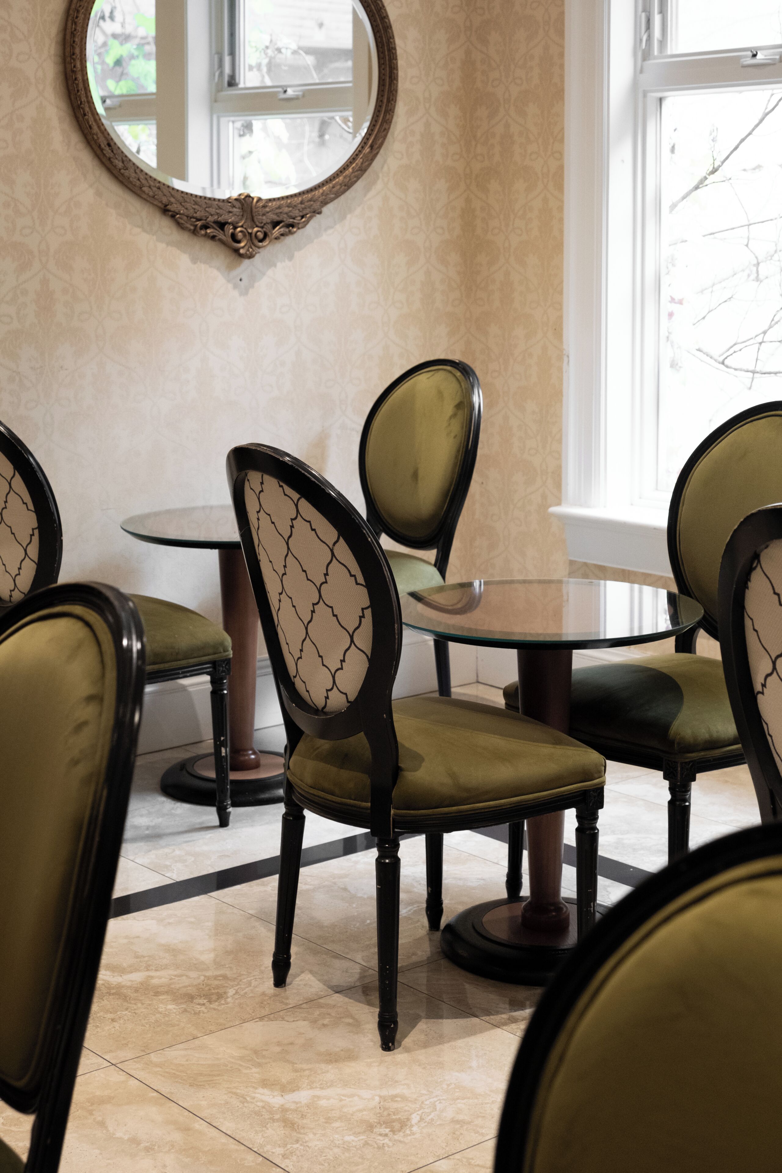A dining area with round tables and chairs, a mirror on the wall, and a window with a view.