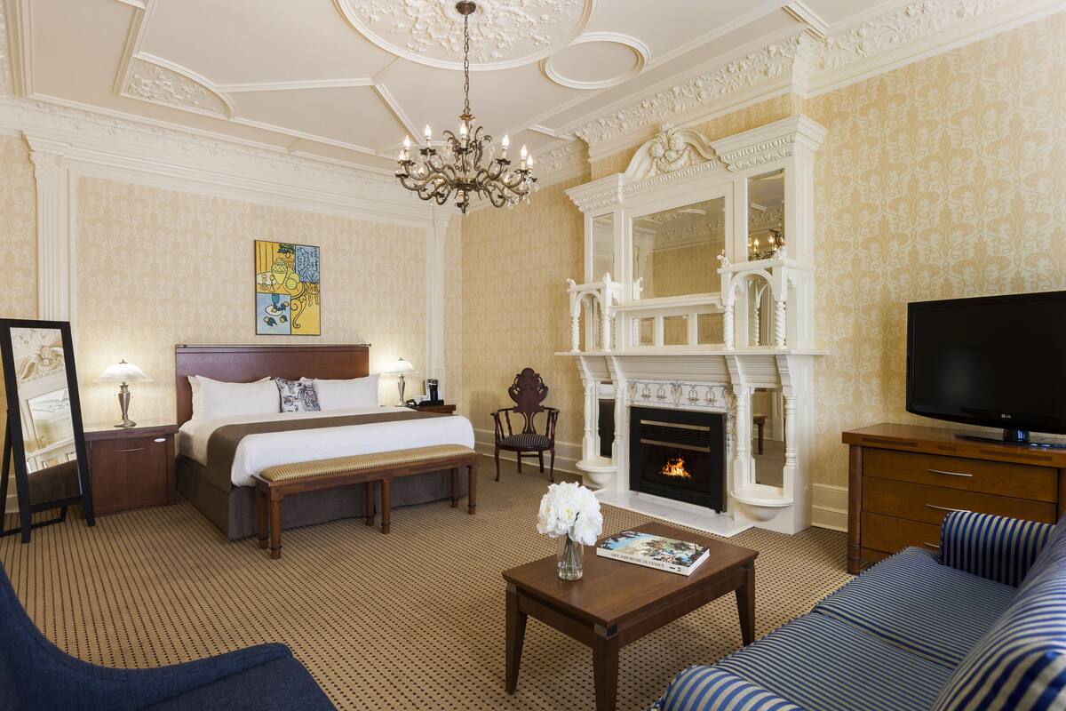 A hotel room with a bed, a sofa, a television, a fireplace, and a chandelier.