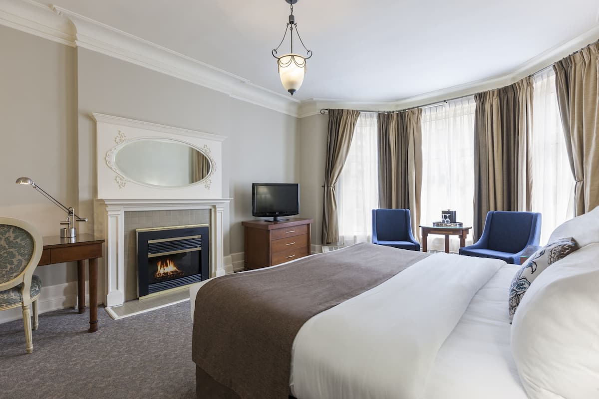 A hotel room with a large bed, a fireplace, a television, two chairs, and a small table.