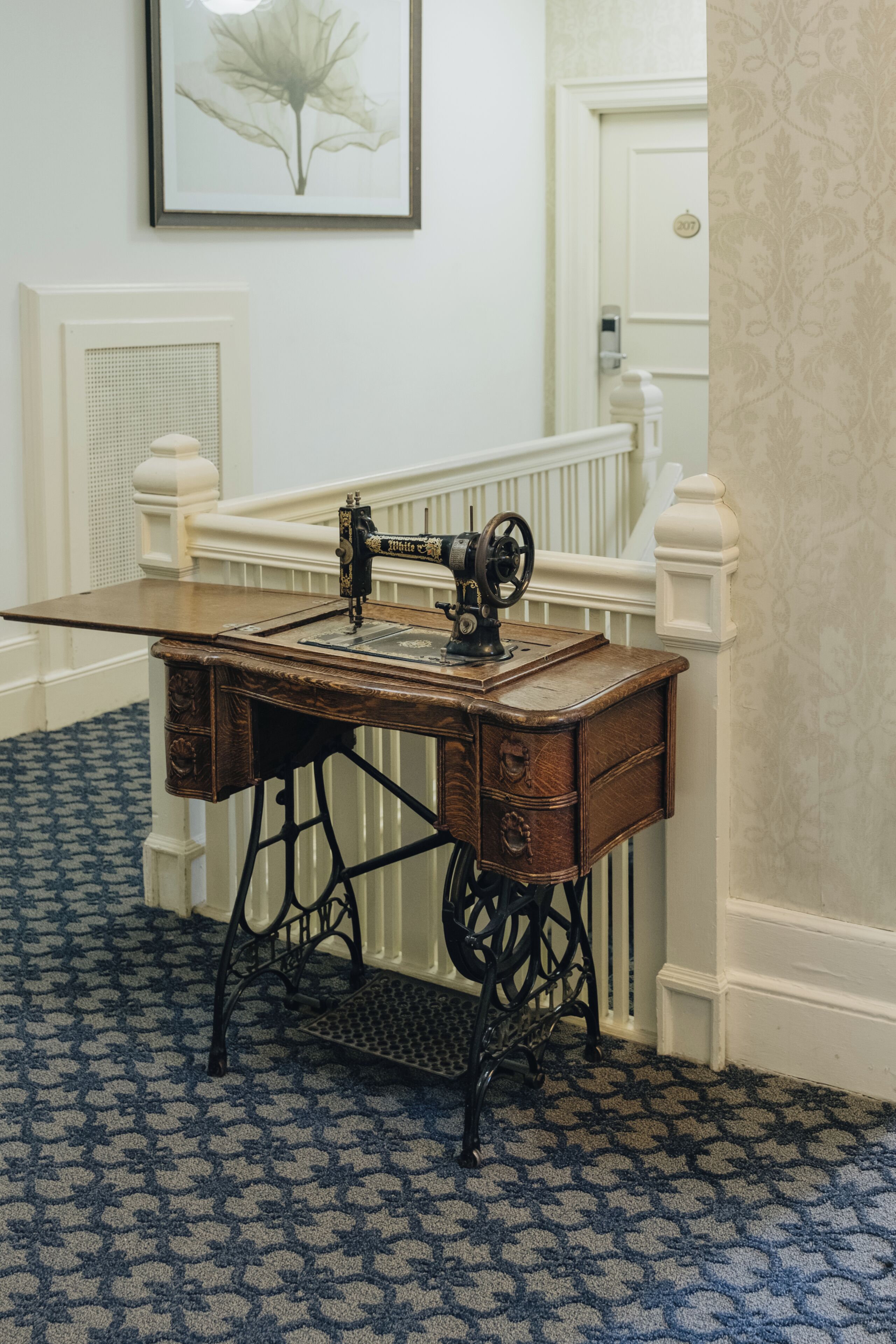A vintage sewing machine on a wooden table in a room with patterned carpet and white walls.