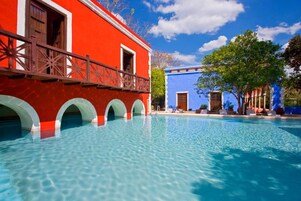 A swimming pool with clear blue water, a red building with white arches, and a blue building with a door.