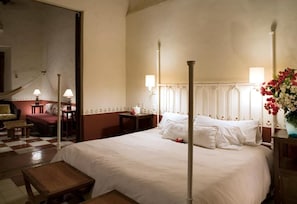 A hotel room with a large bed, a sitting area with a chair and table, and a decorative vase with flowers. - Hacienda Santa Rosa de Lima (Santa Rosa)