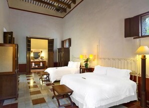 A hotel room with two beds, a wooden bench, a desk with a lamp, and a view of the outside through a window. - Hacienda Santa Rosa de Lima (Santa Rosa)