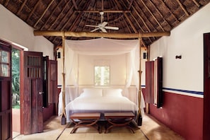 A room with a bed under a canopy, a ceiling fan, and a window with curtains.