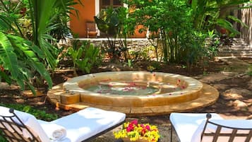 Un jacuzzi rodeado de exuberante follaje, con dos sillones de descanso y un arreglo floral en primer plano.