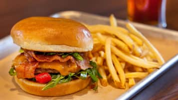 Una hamburguesa con tocino, queso y lechuga, acompañada de una porción de papas fritas en un plato.