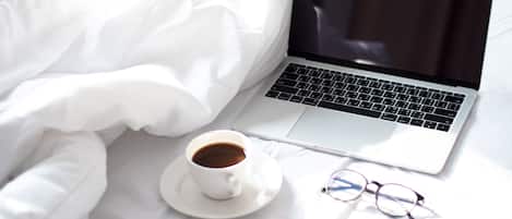 A laptop on a bed with a cup of coffee and glasses.