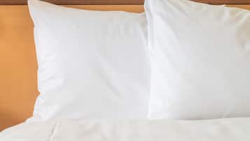 A bed with white bedding and pillows against a wooden headboard.