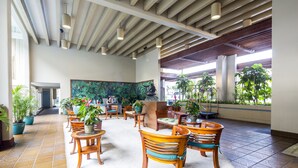 A spacious lobby with wooden chairs and tables, a reception desk, and large windows allowing natural light.