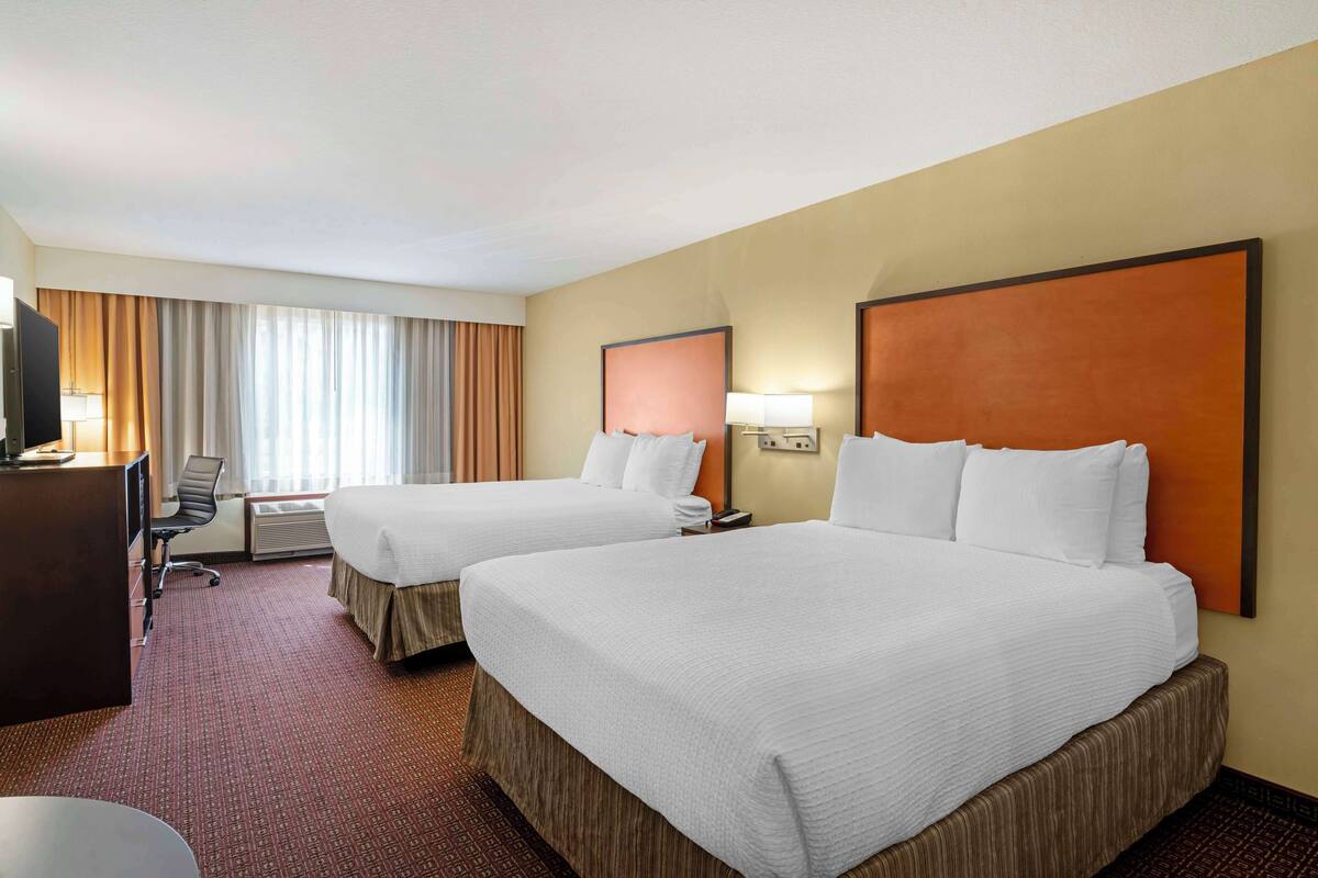 Une chambre d’hôtel avec deux lits, un bureau, une chaise et un téléviseur.