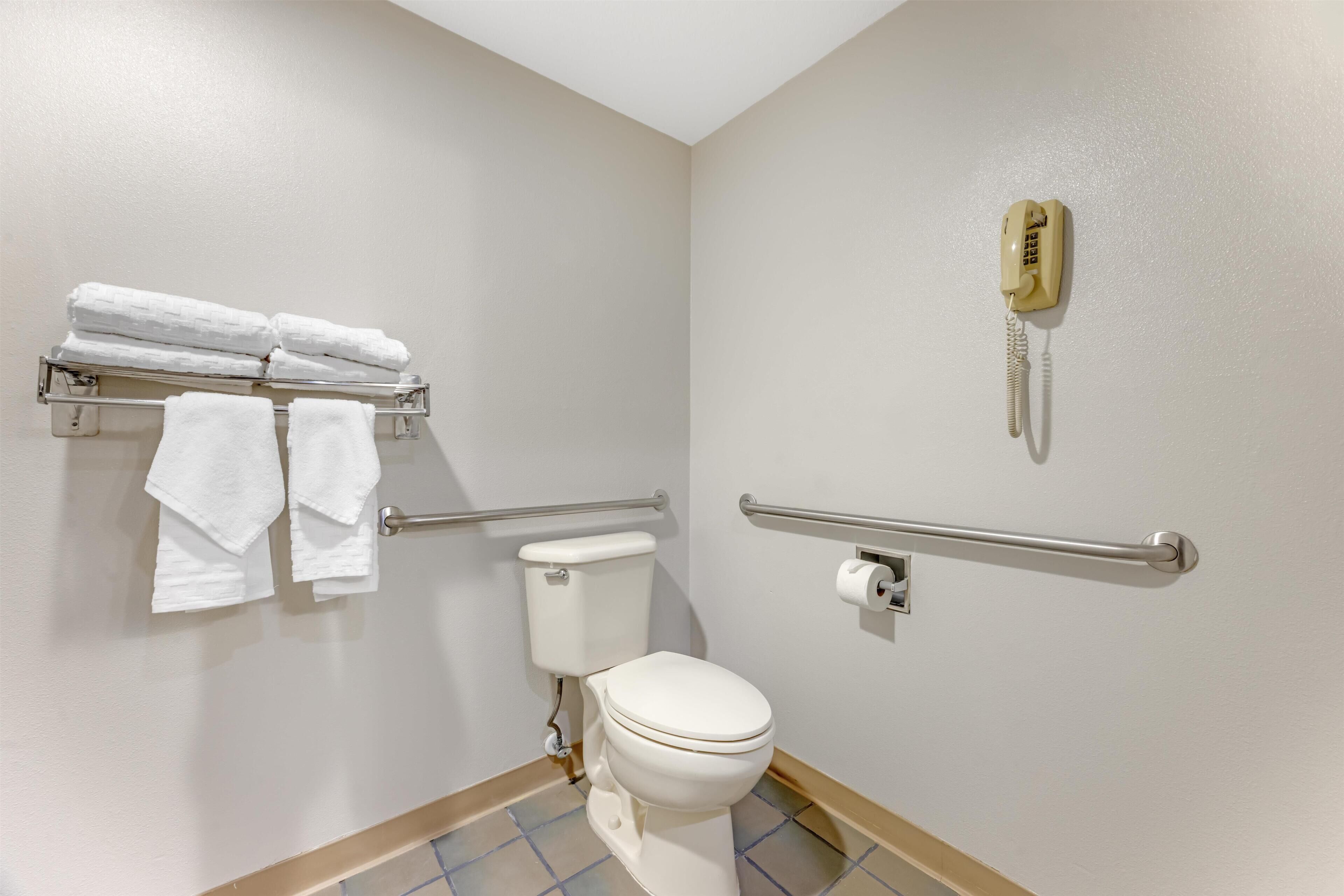 Un baño con inodoro, barra de apoyo, toallero y teléfono.