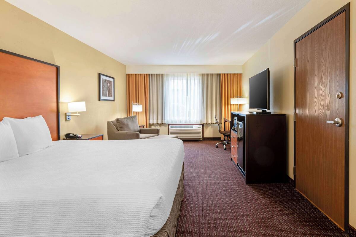 Une chambre d’hôtel avec un grand lit, un bureau avec une télévision, une chaise et une armoire.