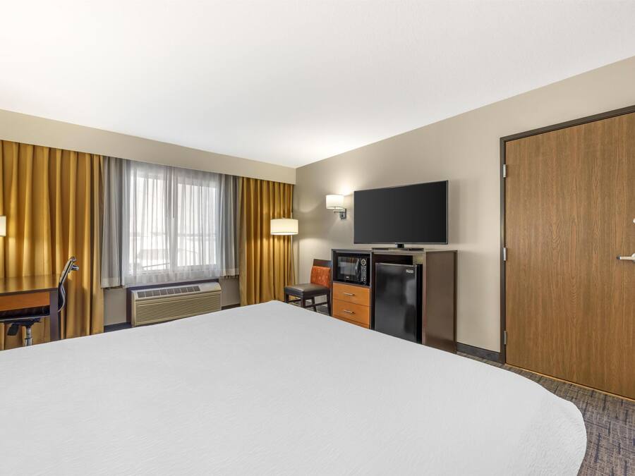Una habitación de hotel con una cama grande, un escritorio con silla, televisión, minibar y una puerta de madera.